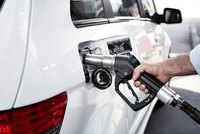 Eine Person tankt Benzin in ein weißes Auto. Die Tanksäule ist im Bild sichtbar, während der Tankdeckel geöffnet ist. Der Fokus liegt auf dem Tankstutzen, der in den Tank des Fahrzeugs gesteckt wird.