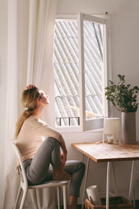 Eine Frau sitzt auf einem Stuhl neben einem geöffneten Fenster