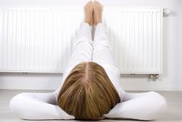 Eine Person mit langen, braunen Haaren liegt in weißer Kleidung entspannt auf dem Boden, die Füße an einer Heizkörperwand abgestellt. Die Körperhaltung zeigt eine entspannte Stimmung.