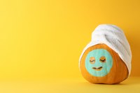 Ein orangefarbener Kürbis mit einem lächelnden, bemalten Gesicht und geschlossenen Augen. Er trägt ein weißes Handtuch auf dem Kopf und steht vor einem gelben Hintergrund. Der Kürbis vermittelt eine entspannte, fröhliche Stimmung.