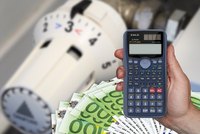 Eine Hand hält einen Taschenrechner, während im Hintergrund ein Thermostat und Geldscheine zu sehen sind. Das Bild vermittelt das Thema Energieeinsparung und Kostenkontrolle.